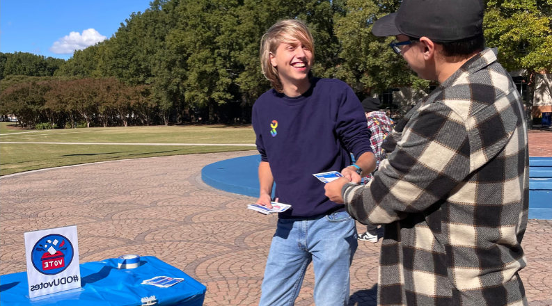 A student hands out a flyer to another student on ODU's campus.